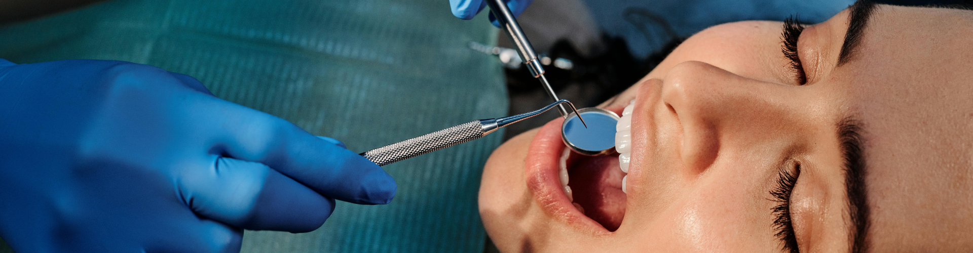 Gloved hands using dental tools in woman's mouth.